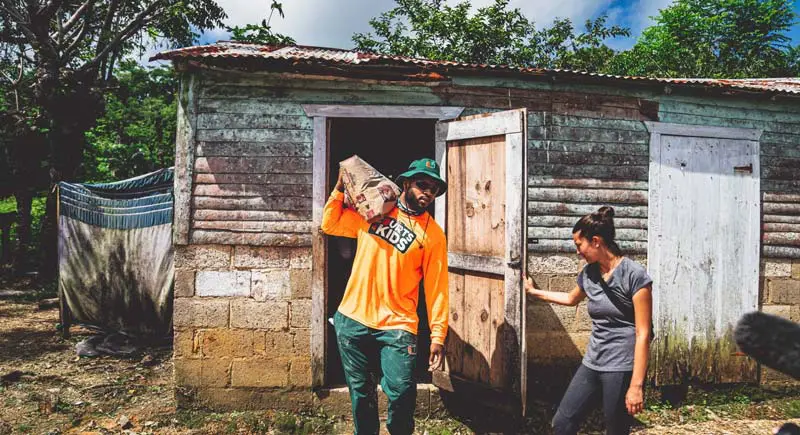 A woman holding a door for a man carrying a bag on his shoulder