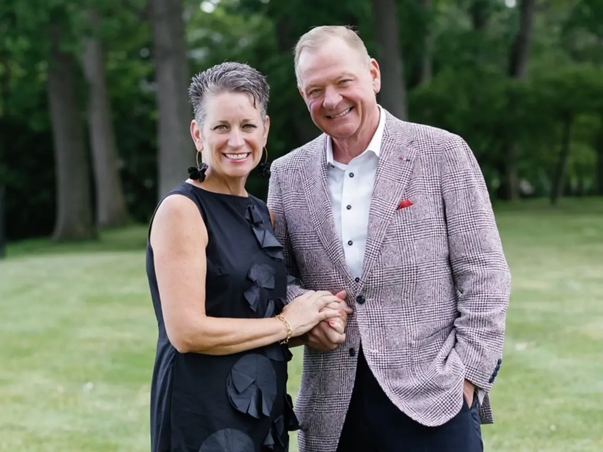 A woman holding a door for a man carrying a bag on his shoulder